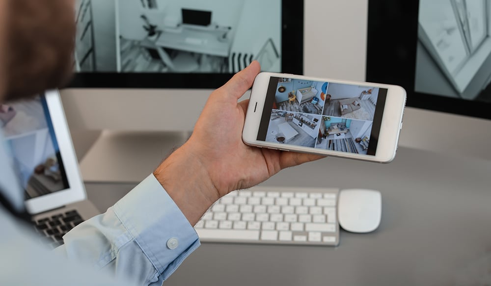 Remote security professional monitoring residential home on his phone with screens in background