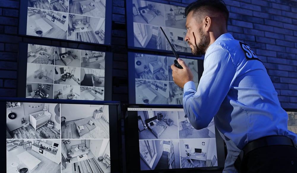 Security worker speaking into walkie talkie looking at security camera feed