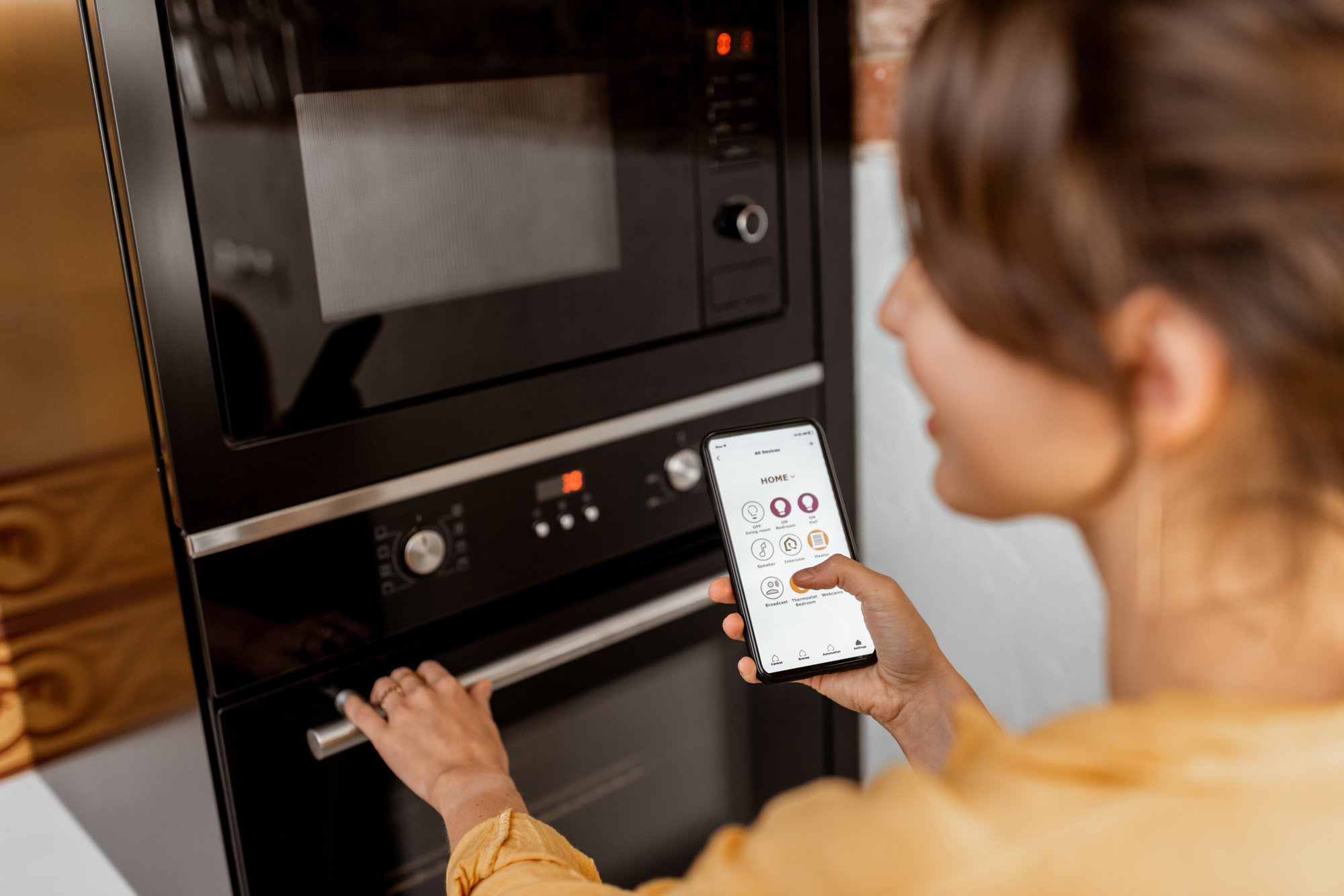 Woman controlling kitchen appliance through app on her phone