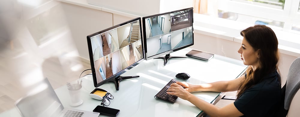 Woman monitoring two security camera monitors in office