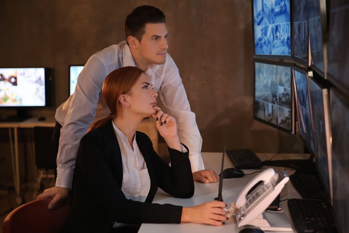 Woman showing man video feed on security monitors